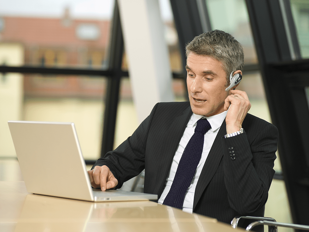 Businessman using a Bluetooth headset connected directly to a laptop computer.