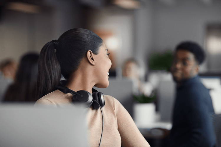 Lady wearing her headset artound her neck leaning back to talk to her colleague.